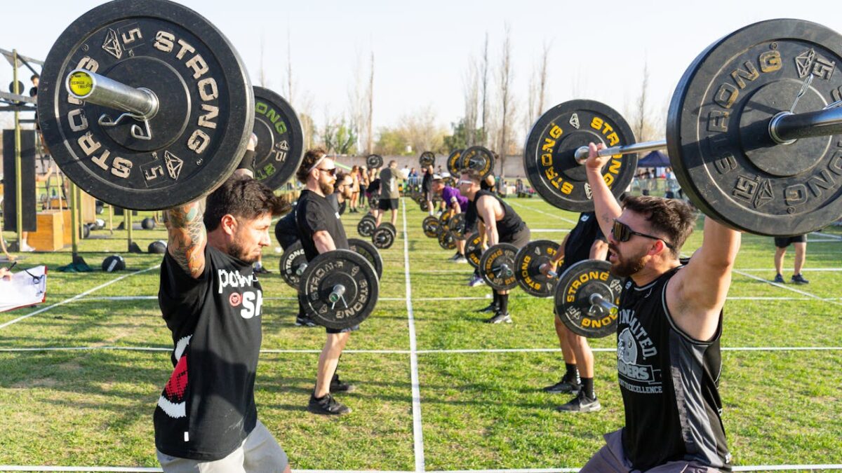 Strong athletes competing in an outdoor weightlifting event, lifting barbells in daylight.